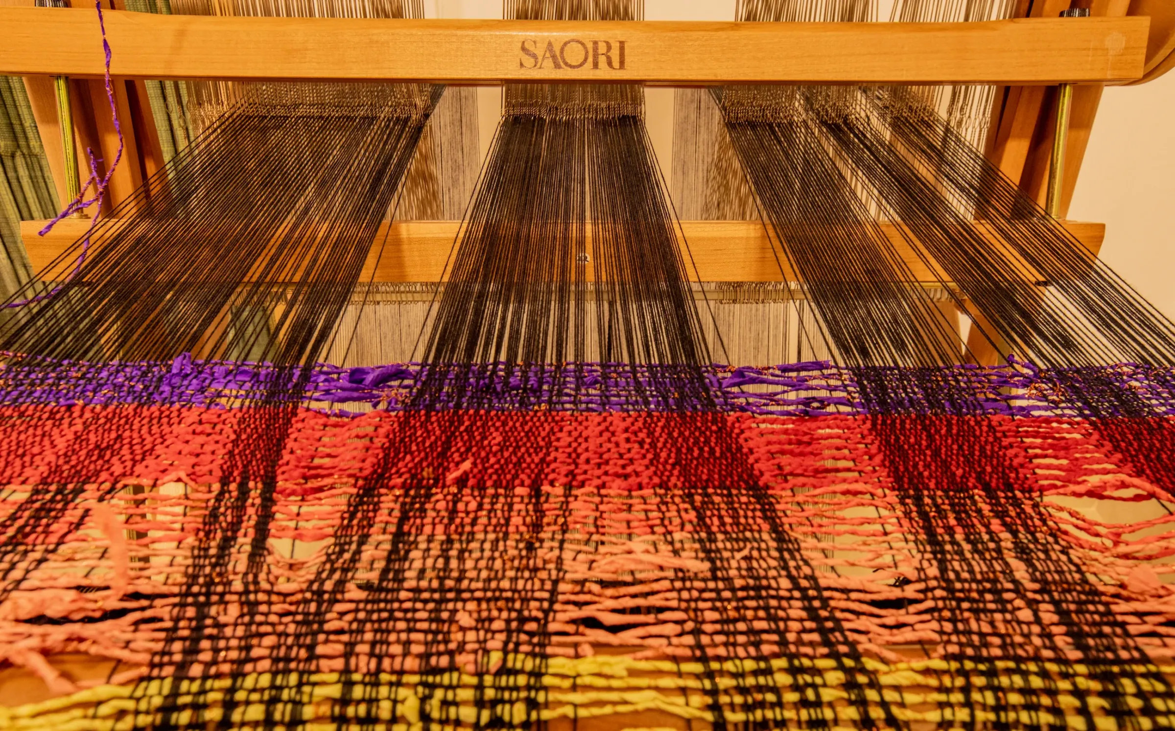 Black warp threads on a SAORI loom above a band of colourful weaving