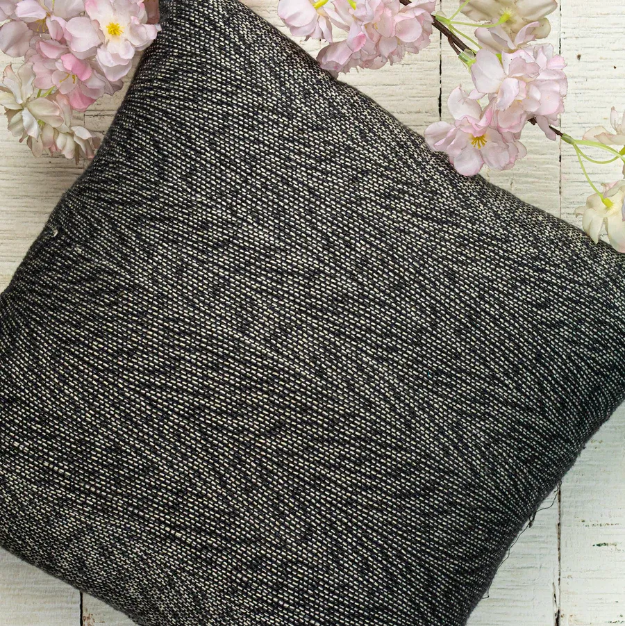 A charcoal handwoven SAORI cushion among pink blossoms