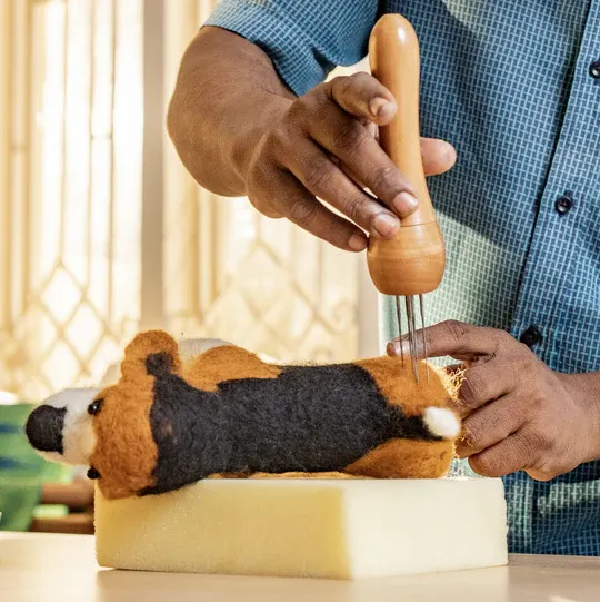 Hands needle felting a small wool dog on a foam block