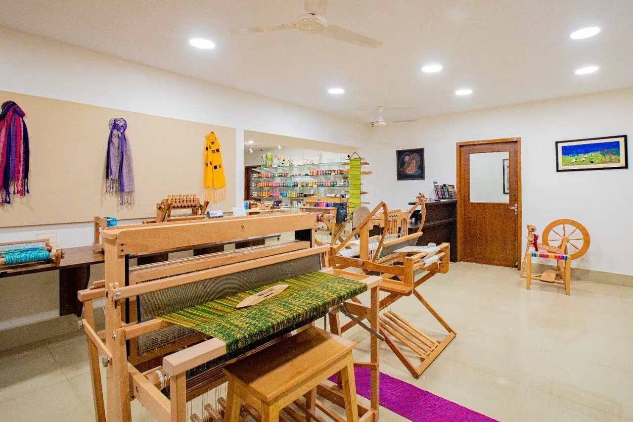 The Shuttles & Needles studio with floor looms, a spinning wheel and handwoven textiles on the walls