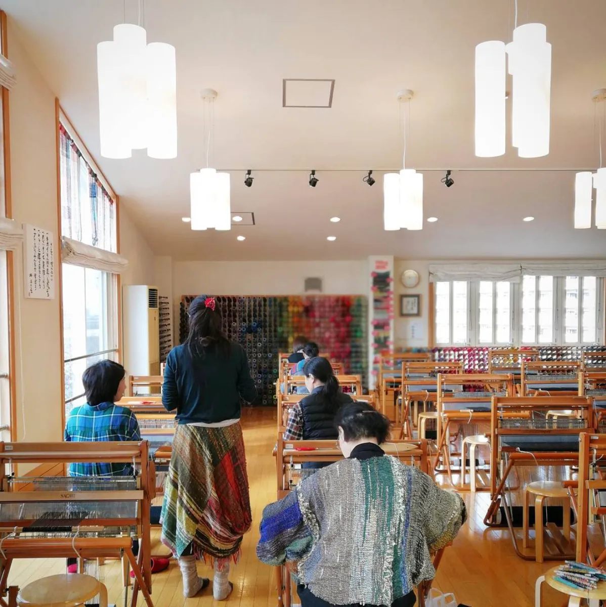 Weavers at SAORI looms in a bright studio lined with shelves of yarn