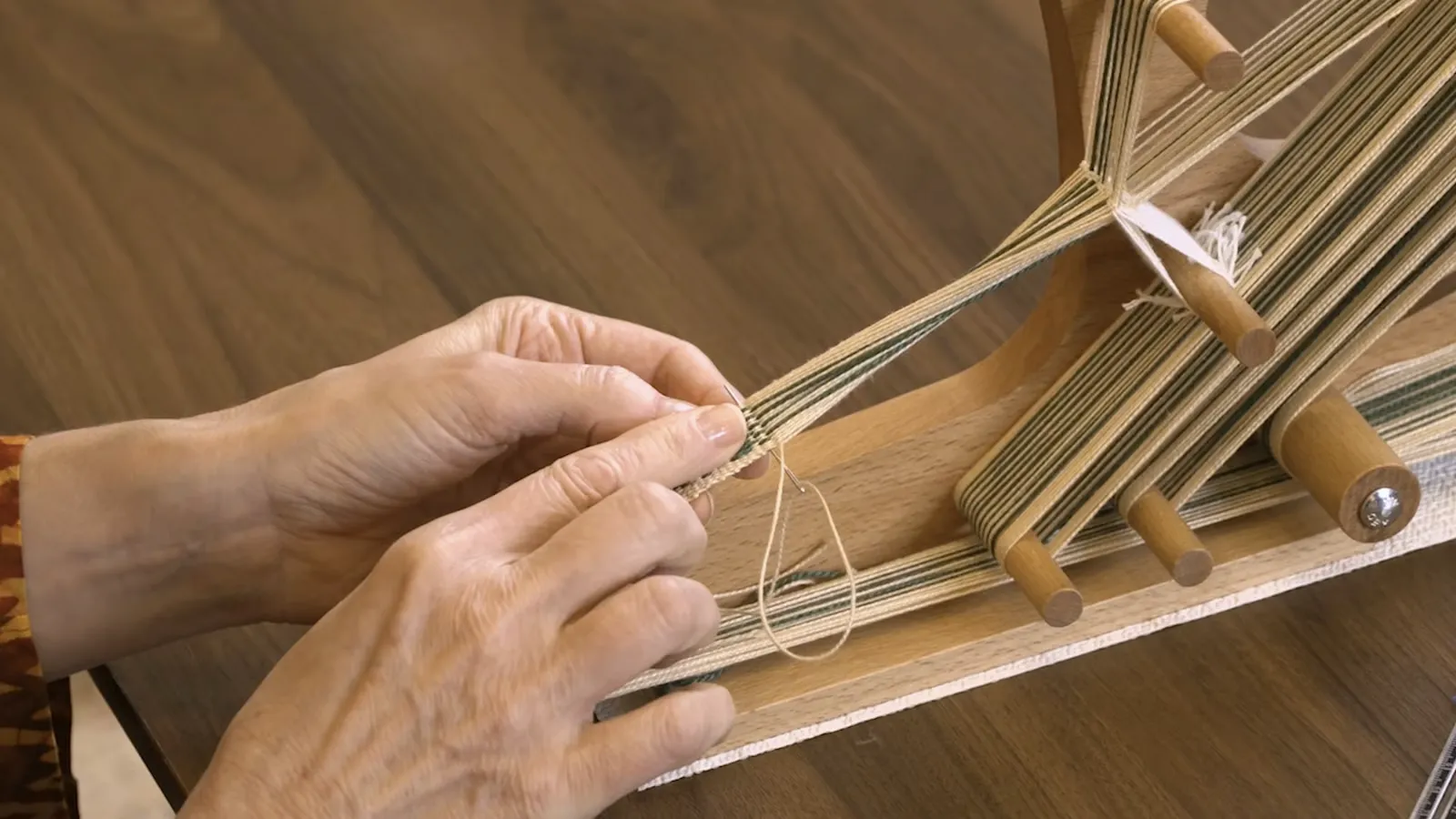 Hands weaving a narrow band on an inkle loom
