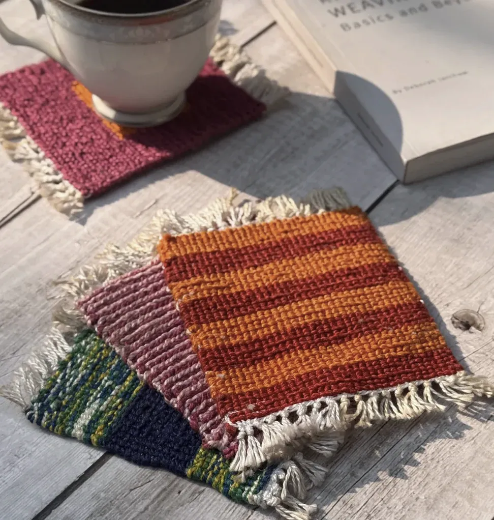 Handwoven coasters in rust, plum and green stacked beside a cup