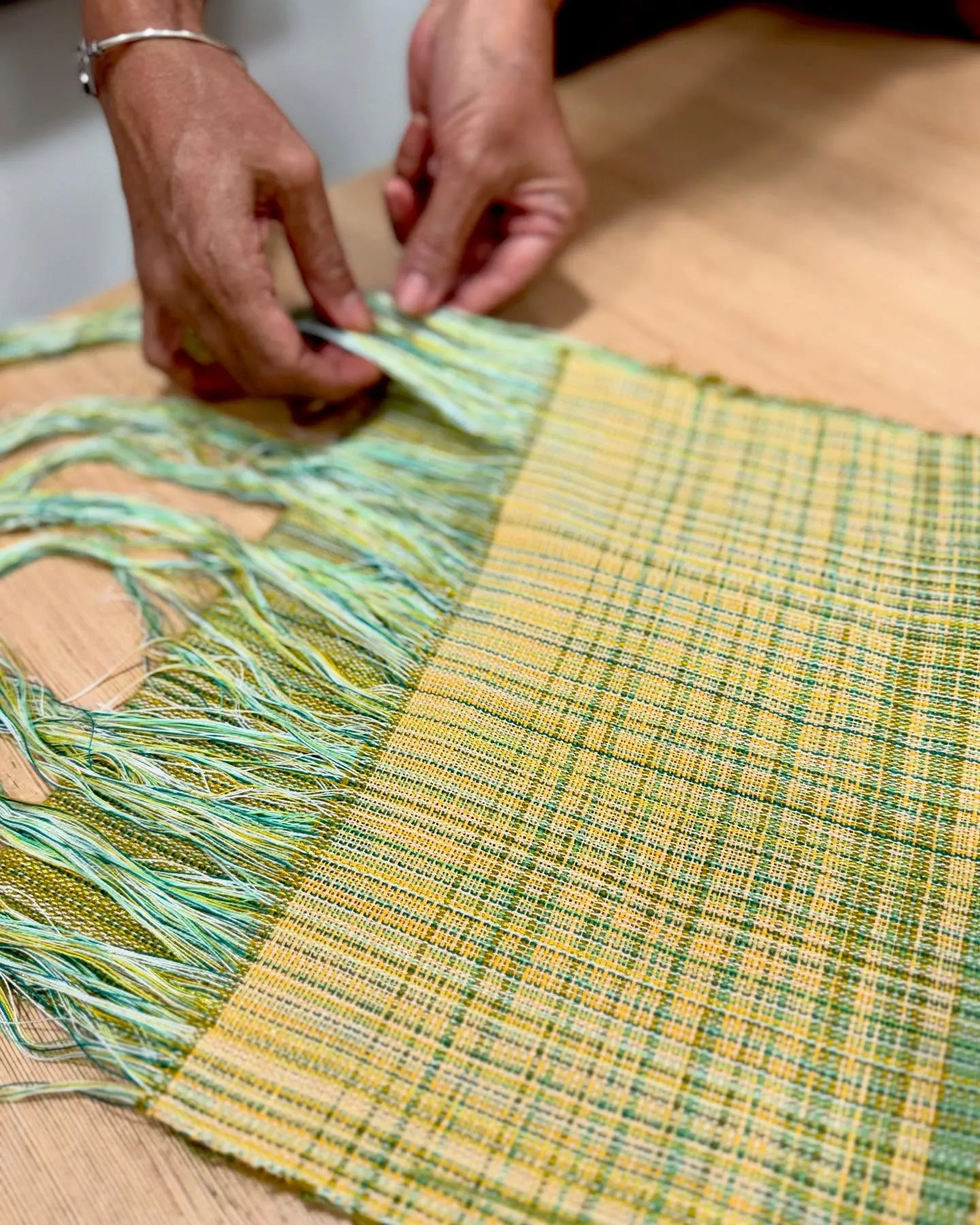Hands tying the fringe of a yellow and green handwoven cloth