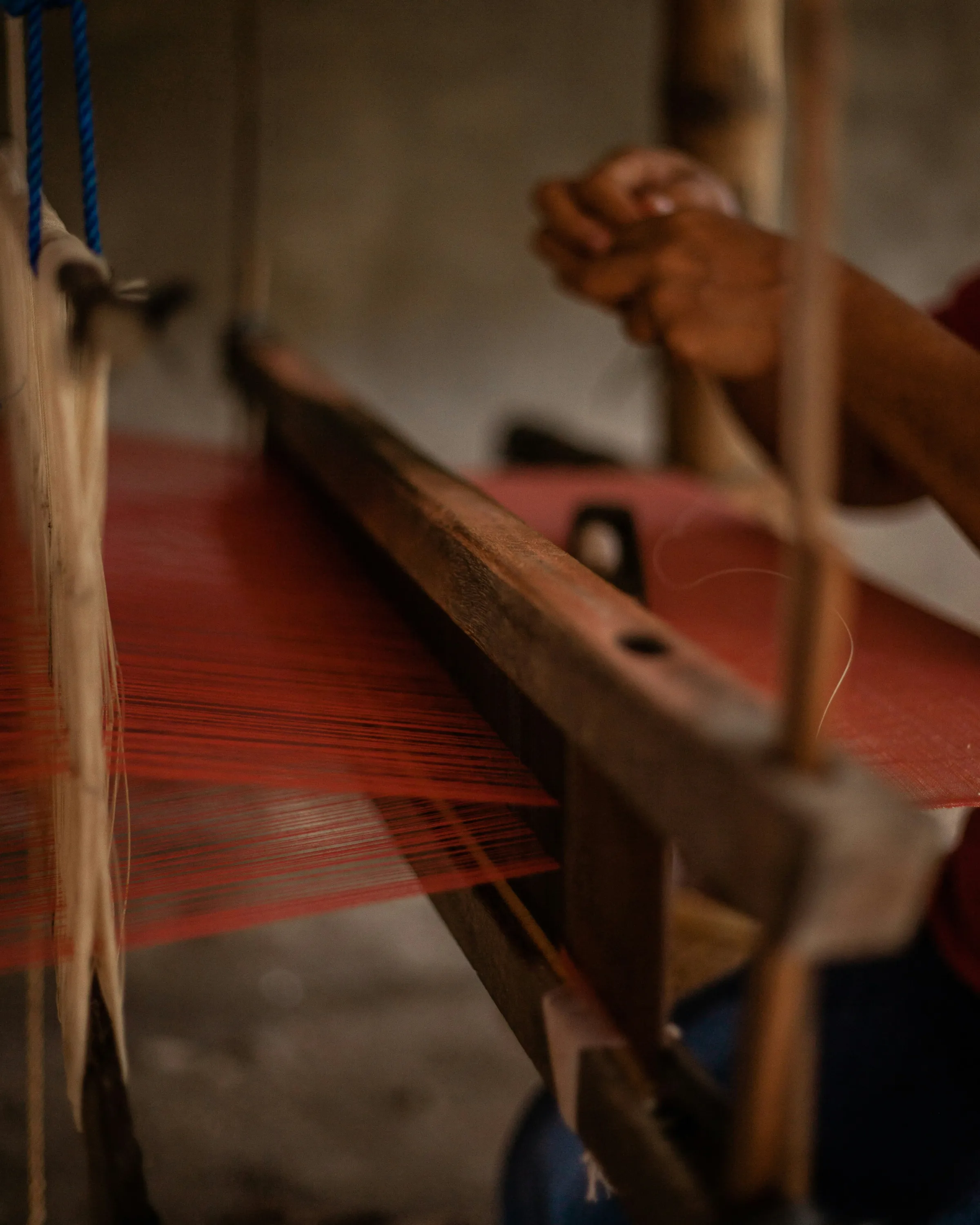 Close-up of a wooden loom with a red warp, softly lit