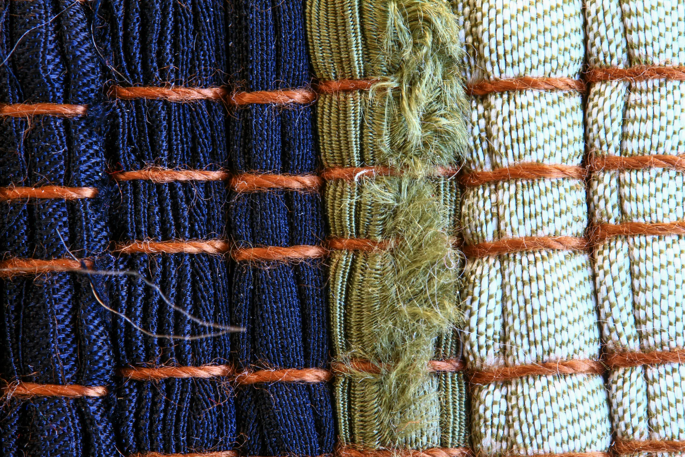Close-up of SAORI weaving in navy, olive and cream with rust-coloured weft and loose tufts