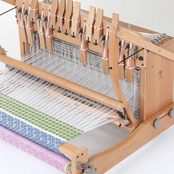 A multi-shaft wooden table loom with woven samples in green, blue and pink
