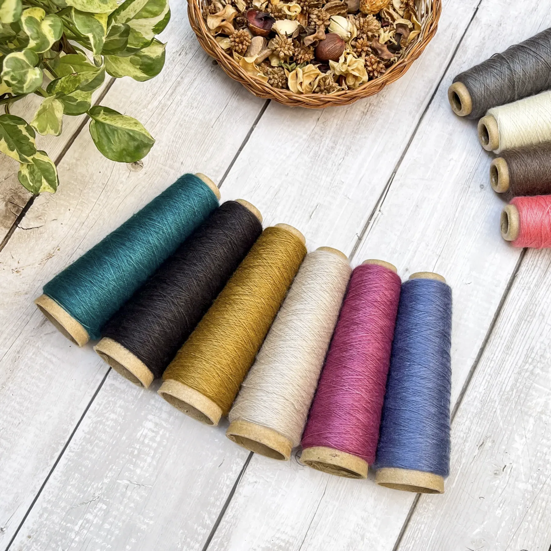 Mini-cones of yarn in teal, black, mustard, cream, pink and blue on a white wooden table