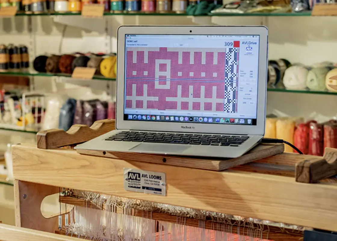 A laptop showing a weave draft on top of a computer-controlled dobby loom