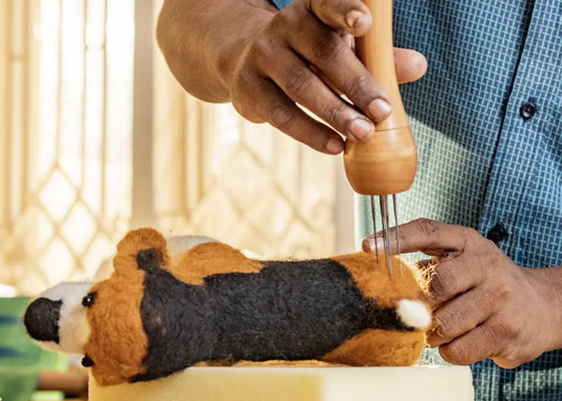 Hands shaping a needle-felted dog with a felting tool
