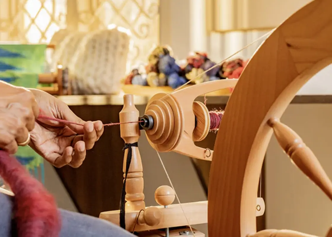 Hands drafting red fibre onto a wooden treadle spinning wheel