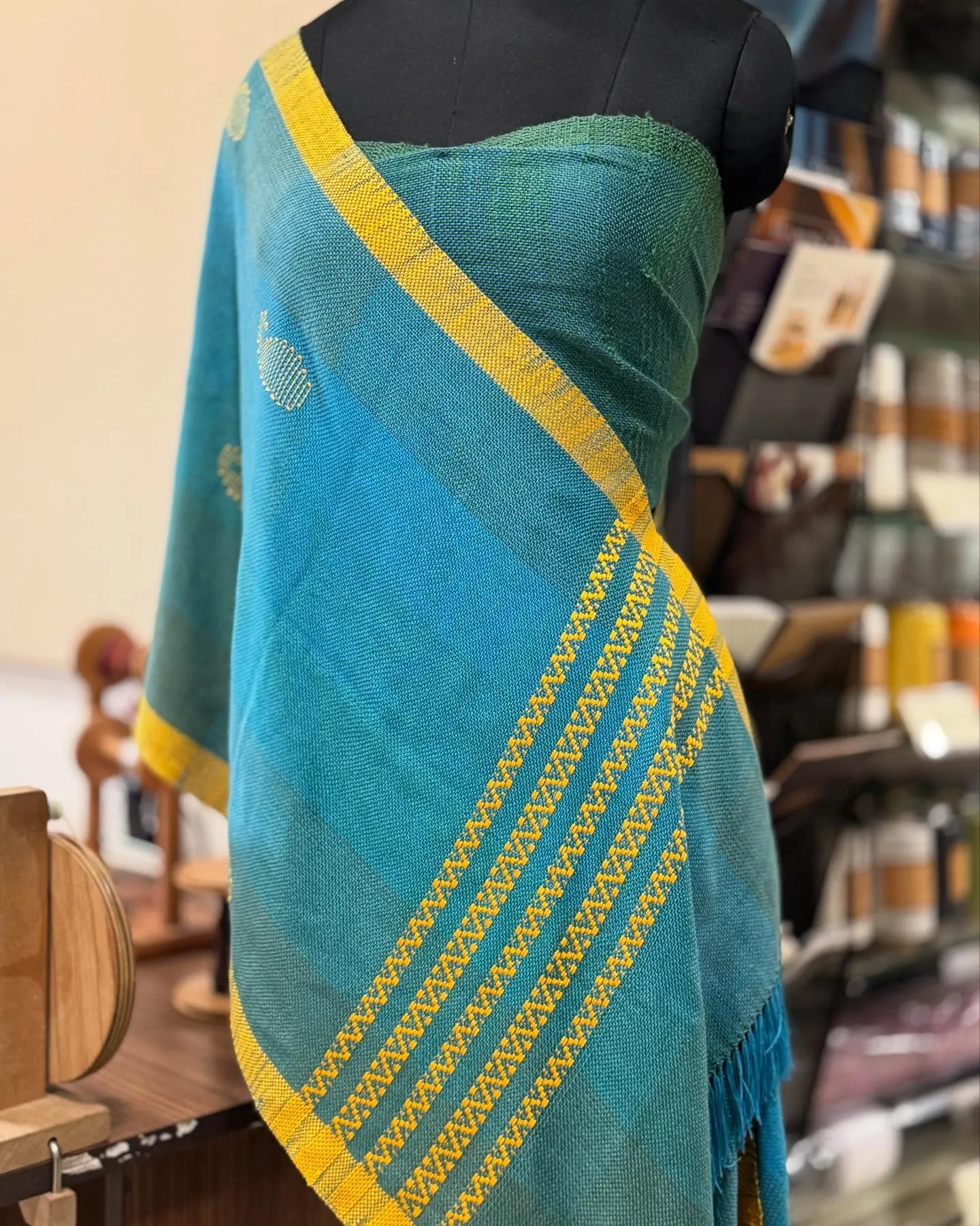 A teal saree with gold stripes draped on a stand in the studio