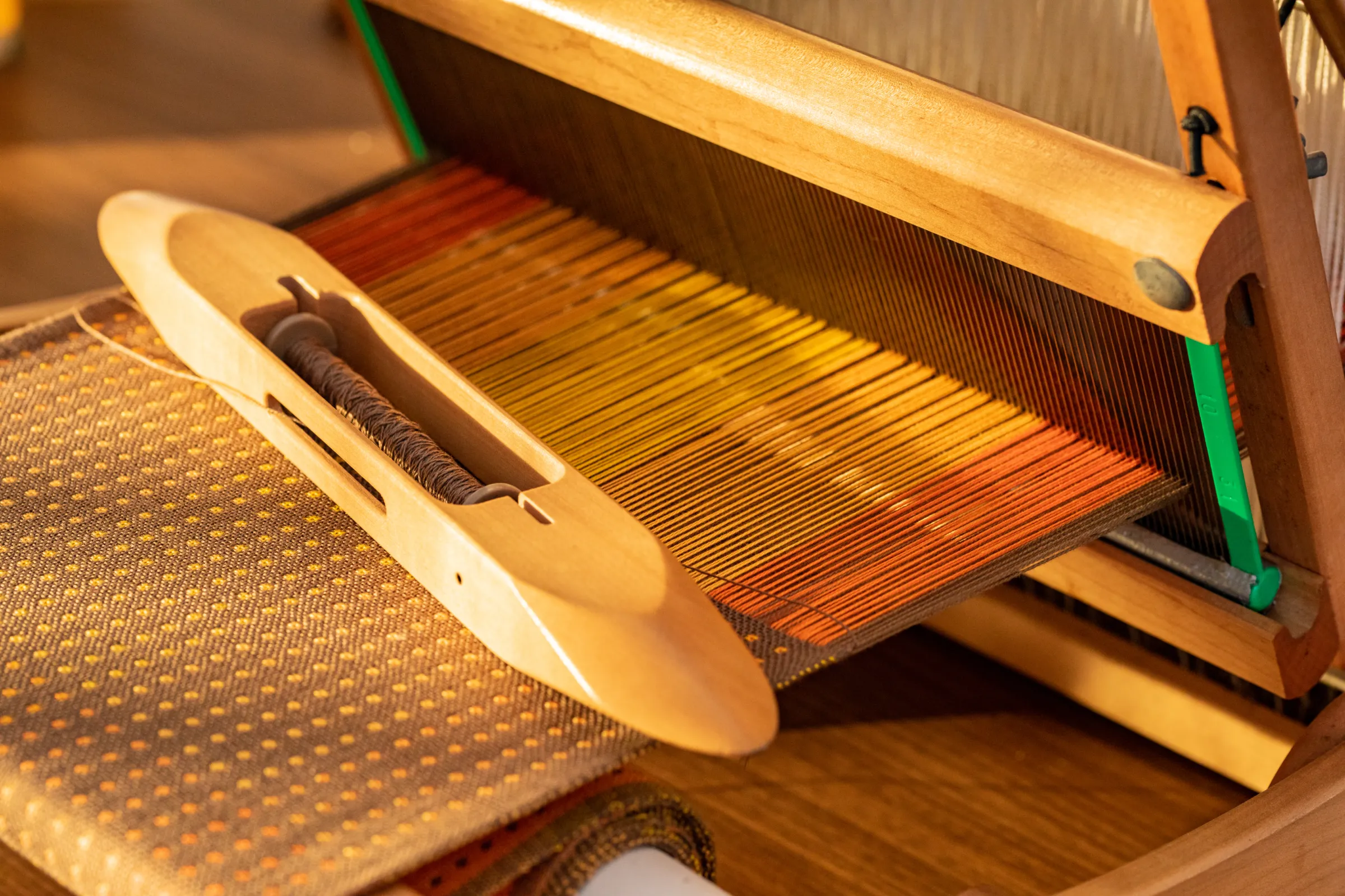 A wooden boat shuttle resting on the cloth of a table loom