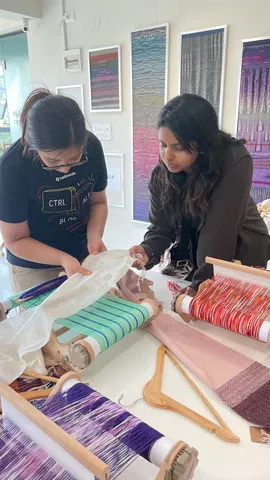 Two students look closely at a warp on a rigid heddle loom