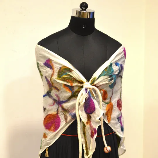 A white nuno-felted shawl with colourful leaf shapes on a dress form