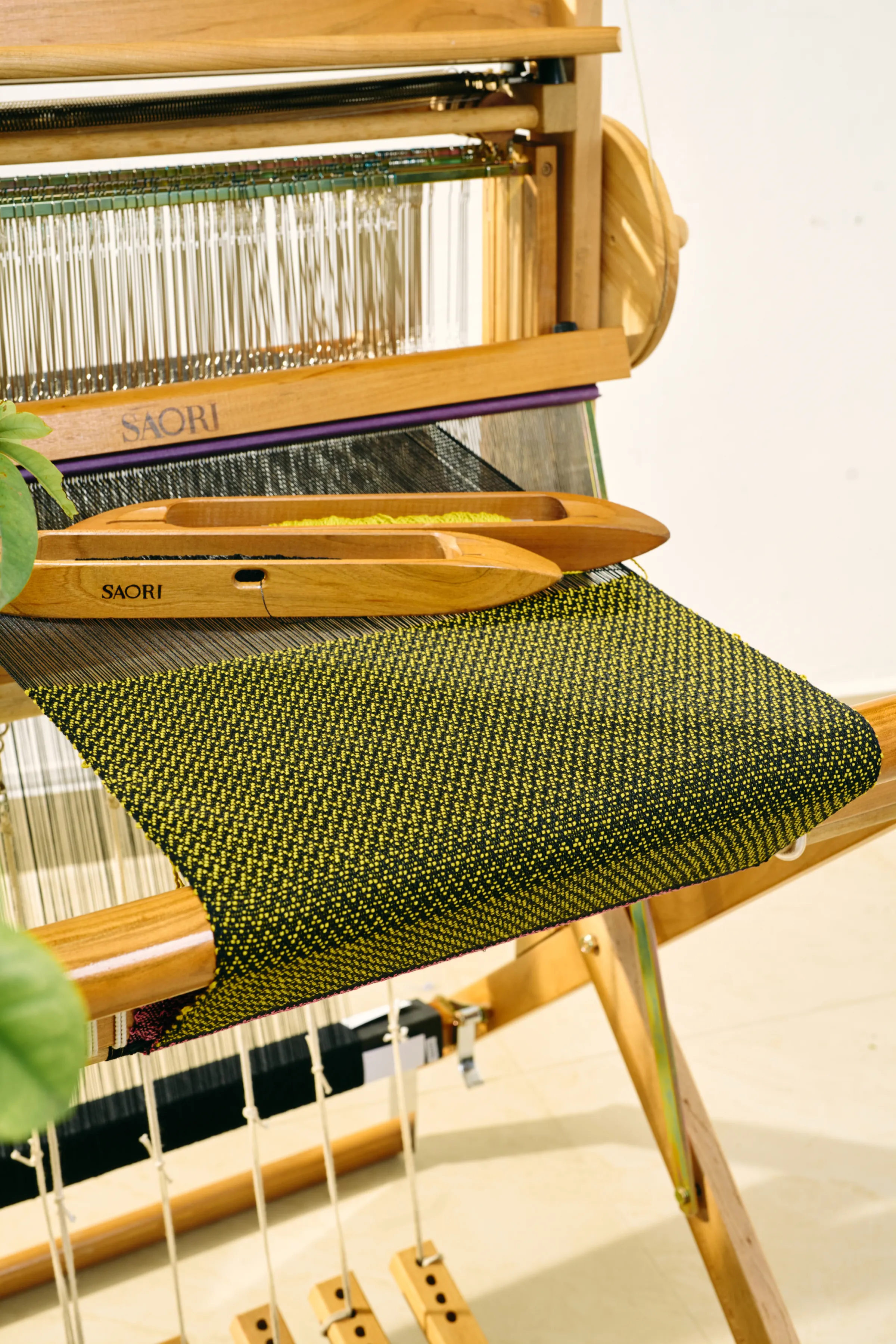 Two SAORI shuttles resting on green handwoven cloth on a SAORI loom