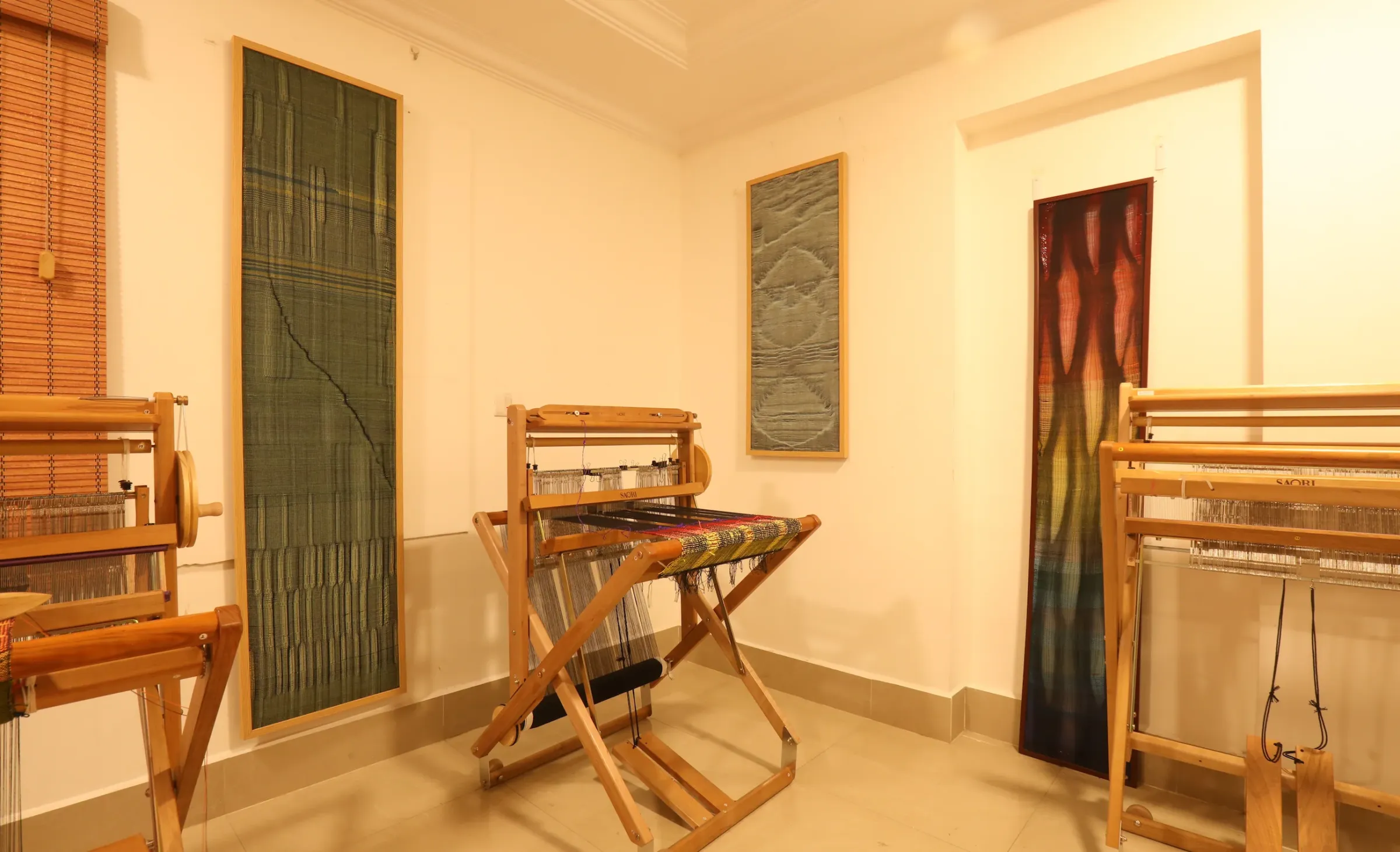Wooden looms in the warm light of the studio, with handwoven hangings on the walls