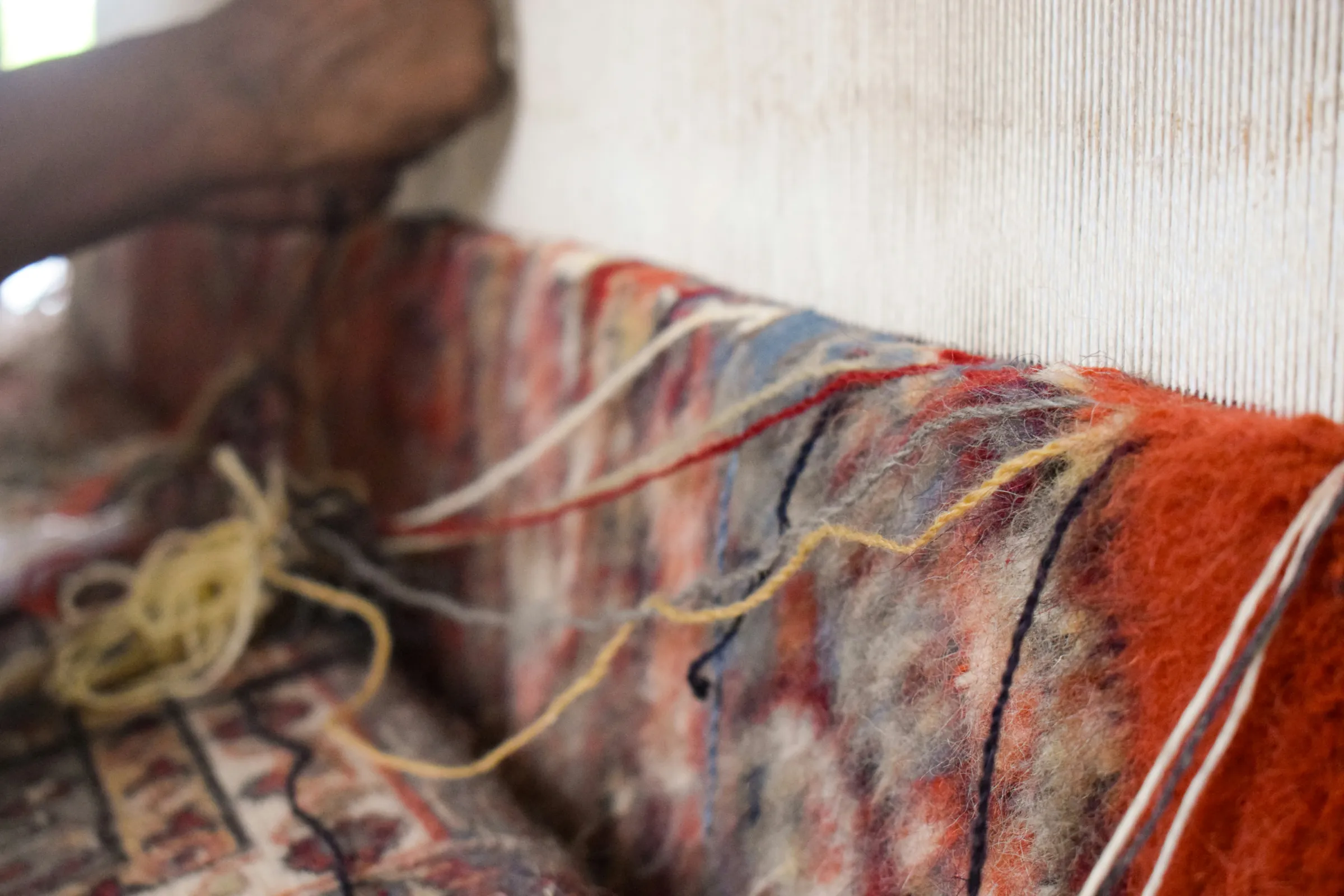 Close-up of felted wool in red, orange and cream beside the warp of a loom