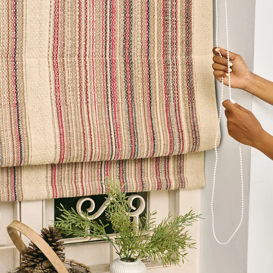 A handwoven striped roman blind being raised over a window