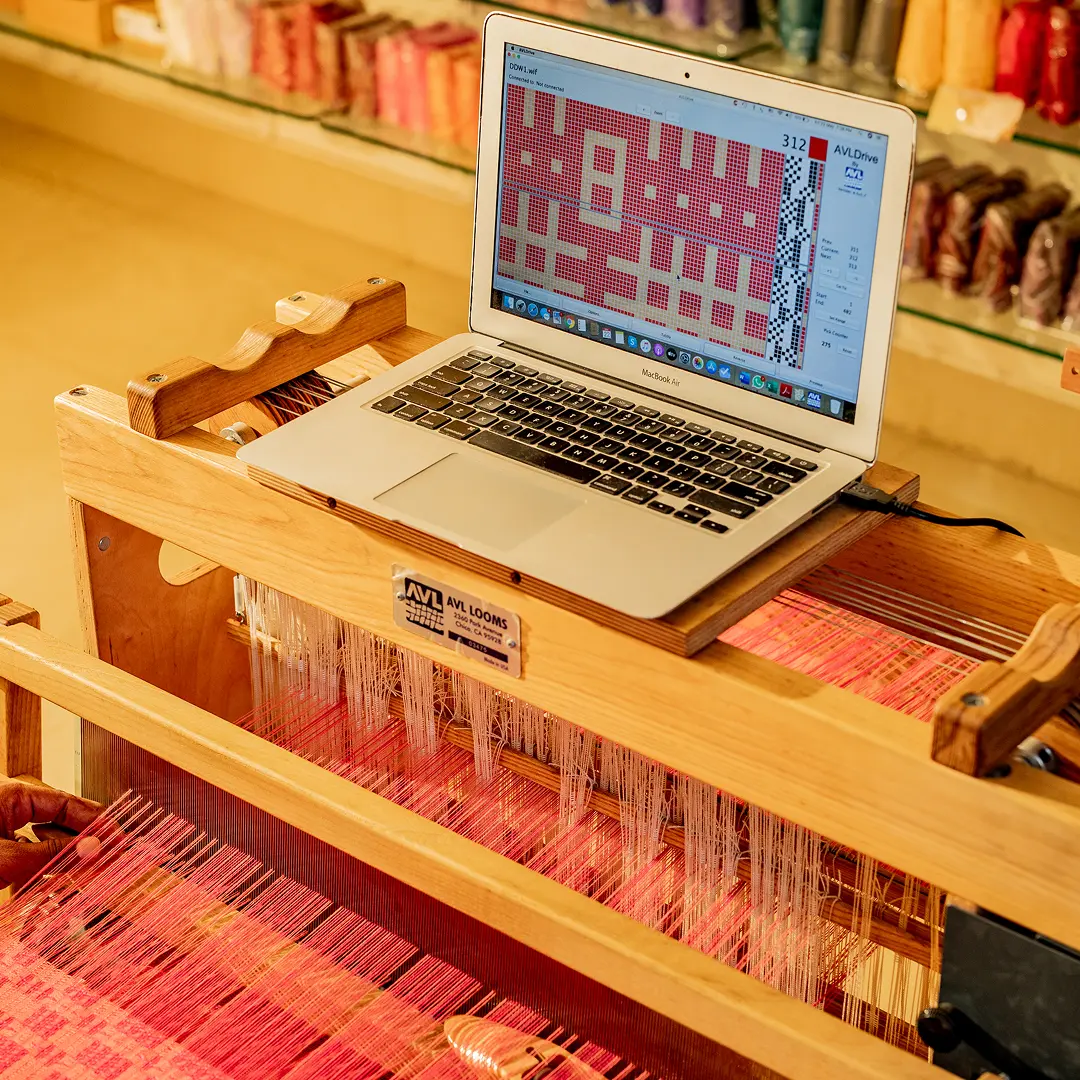 A laptop showing a weave draft on a computer-controlled dobby loom warped in red and pink