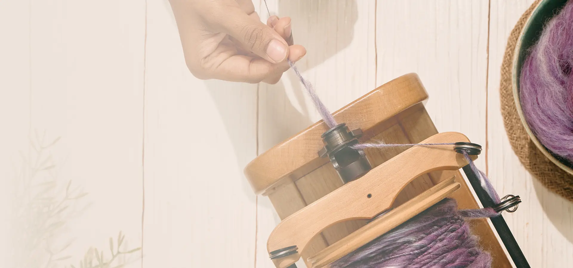 A hand drawing purple yarn onto the bobbin of an electric spinning wheel beside a bowl of fibre