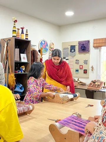 A teacher helps a young girl weave on a small table loom in the studio