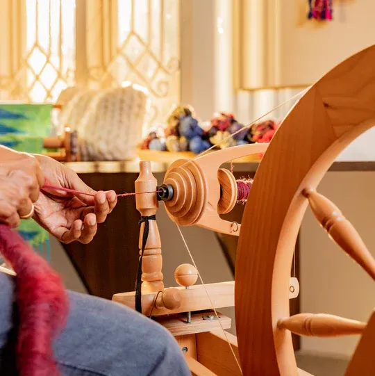 Hands spinning red fibre into yarn on a treadle spinning wheel