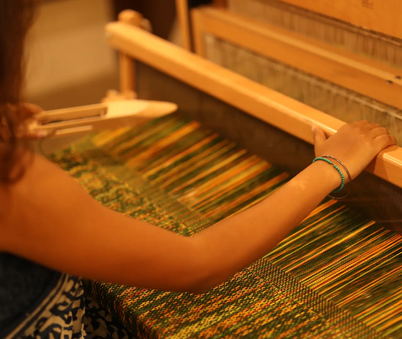 A weaver working at a floor loom with a green and gold warp
