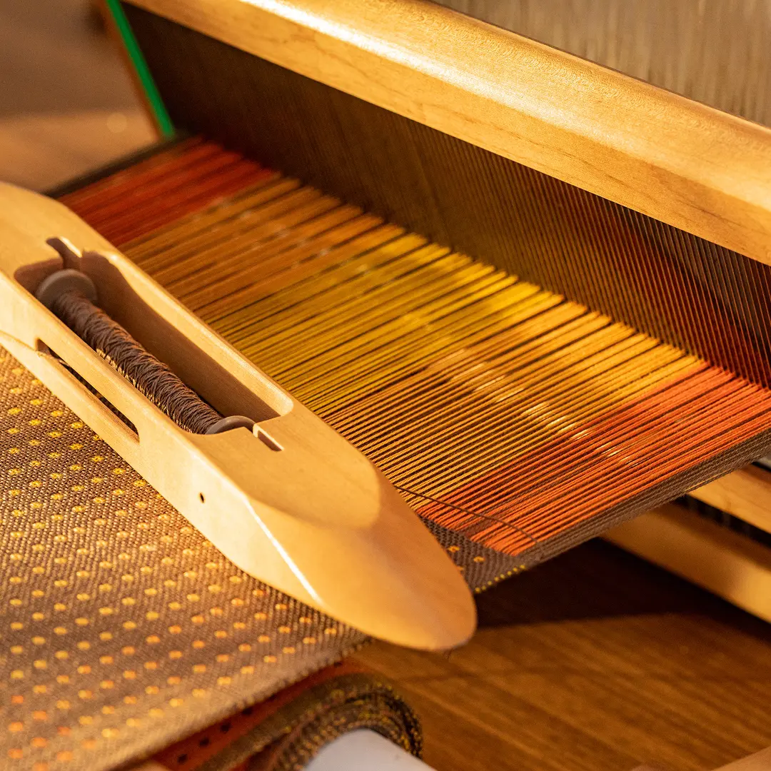 Close-up of a boat shuttle on a table loom with orange and yellow warp threads