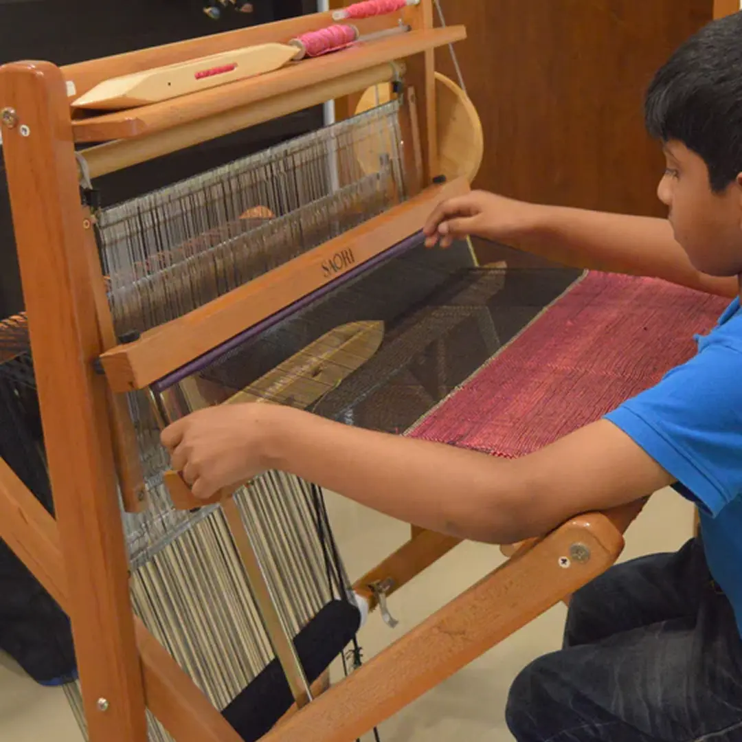A student weaving on a floor loom during a school visit